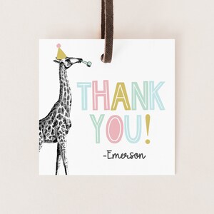 May include: A white thank you tag with a black and white illustration of a giraffe wearing a pink and yellow party hat. The text "THANK YOU!" is in colorful outlined letters. The tag is signed "Emerson".