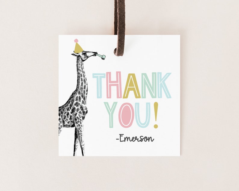 May include: A white thank you tag with a black and white illustration of a giraffe wearing a pink and yellow party hat. The text "THANK YOU!" is in colorful outlined letters. The tag is signed "Emerson".