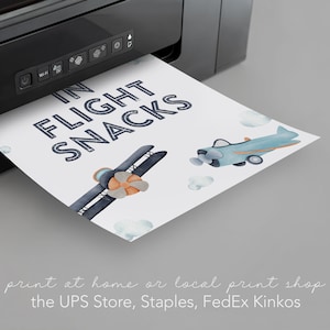 以下が含まれることがあります： 青と白の文字で「IN FLIGHT SNACKS」と書かれた印刷可能な看板。看板には、青と白の飛行機2機と雲を背景にした水彩画のイラストが描かれている。看板は白黒のプリンターで印刷されている。