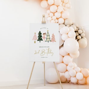 May include: Welcome to Amelia's Tutu Cute 2nd Birthday party sign featuring a ballerina in a pink tutu standing in front of three Christmas trees decorated with gold stars and lights. The sign is on a wooden easel.