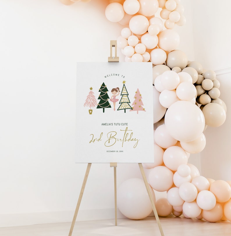May include: Welcome to Amelia's Tutu Cute 2nd Birthday party sign featuring a ballerina in a pink tutu standing in front of three Christmas trees decorated with gold stars and lights. The sign is on a wooden easel.