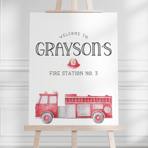 May include: A white rectangular sign featuring the black text WELCOME TO GRAYSON'S FIRE STATION NO. 3, a small red firefighter helmet illustration, and a watercolour-style red fire truck with grey wheels and detailing on a wooden easel.