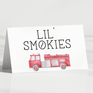 May include: A white folded card featuring the black text LIL' SMOKIES centred above a watercolour illustration of a red fire engine. The fire engine has grey accents, a ladder on top, and a small yellow light on the roof, presented on a white background.