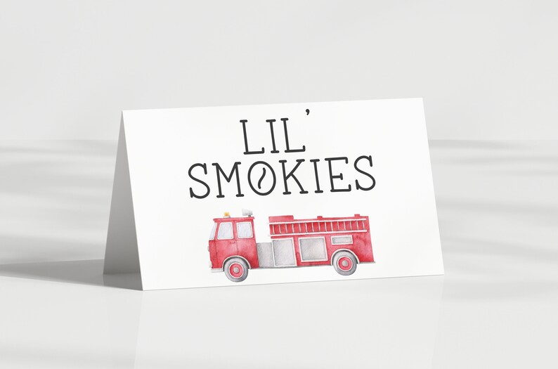 May include: A white folded card featuring the black text LIL' SMOKIES centred above a watercolour illustration of a red fire engine. The fire engine has grey accents, a ladder on top, and a small yellow light on the roof, presented on a white background.