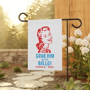May include: A white garden flag with a red and blue graphic of a woman with the text "Grab Him by the Ballot Kamala * 2024".