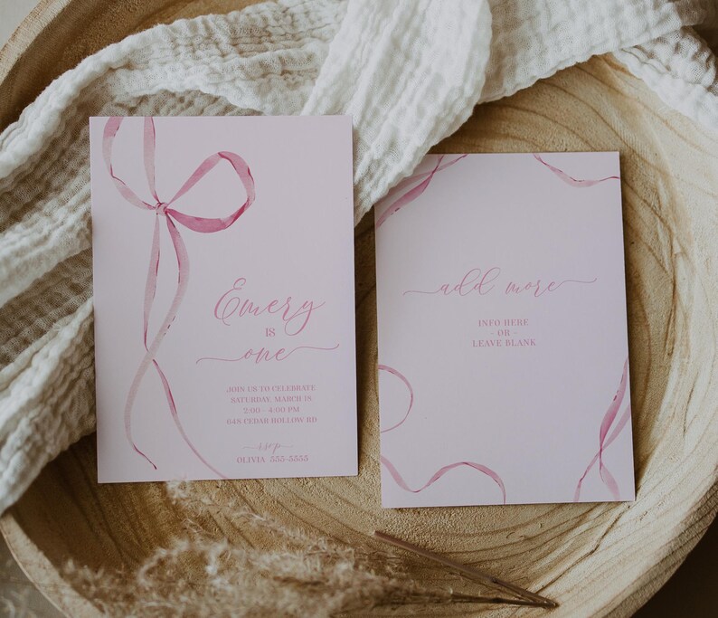 May include: Pink invitation with watercolor ribbons and the text "Emery is one" and details for a birthday party. A second card says "add more" with space to write in.