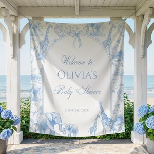 以下が含まれることがあります： 「Welcome to OLIVIA'S Baby Shower」の文字と2028年6月10日の日付が入った、白と青のベビーシャワーバナー。キリン、ゾウ、鳥のイラストが描かれています。バナーは白い構造物に吊るされています。