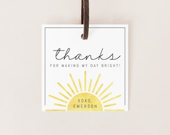 May include: A white thank you tag with a black border and a gold watercolor sun with rays. The text reads "thanks for making my day bright! xoxo, Emerson".