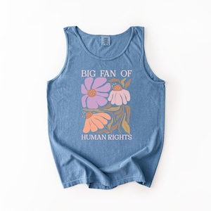 May include: A blue sleeveless tank top featuring a graphic print of three stylized flowers in shades of purple, pink, and orange with brown stems and leaves. The text "BIG FAN OF HUMAN RIGHTS" is printed in white above and below the floral design.
