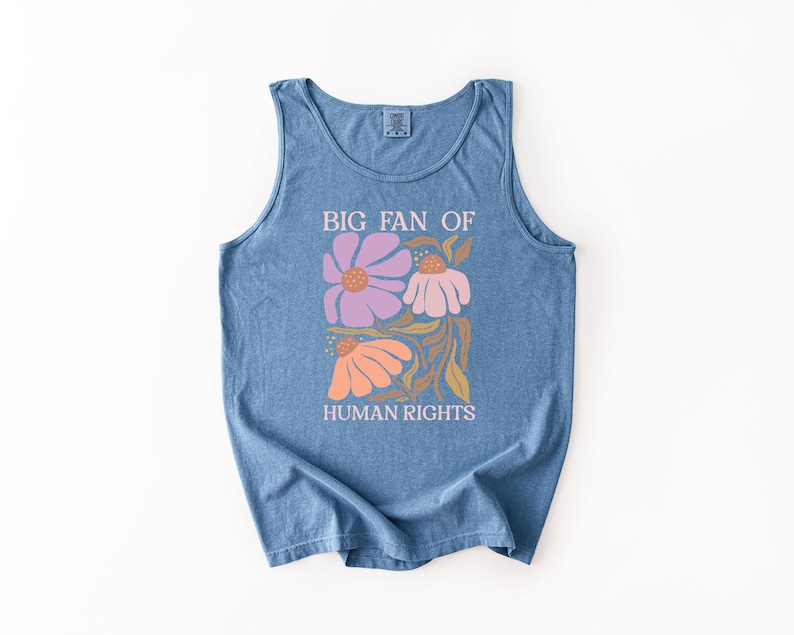May include: A blue sleeveless tank top featuring a graphic print of three stylized flowers in shades of purple, pink, and orange with brown stems and leaves. The text "BIG FAN OF HUMAN RIGHTS" is printed in white above and below the floral design.