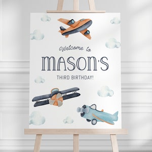 May include: Welcome to Mason's Third Birthday! A white sign with blue and orange watercolour aeroplanes and clouds. The text reads "Welcome to Mason's Third Birthday!"