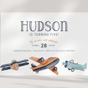 May include: A white birthday invitation card featuring the text HUDSON IS TURNING FIVE! Fly on over and celebrate OCTOBER 28 4:00 PM 2450 Cold Creek Blvd Zionsville, IN RSVP to Co-Pilot Emily at 555-5555 with three watercolor airplanes in blue and orange.