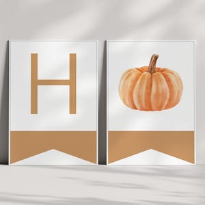 Puede incluir: Dos impresiones artísticas enmarcadas. La impresión de la izquierda presenta la letra "H" en un tono marrón cálido sobre un fondo blanco, con una pancarta a juego en la parte inferior. La impresión de la derecha muestra una calabaza de acuarela con un tallo marrón.