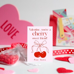 May include: A pink card with red text that reads "Valentine, you're a cherry sweet friend!" with a drawing of two red cherries with a red ribbon. The card is signed "from: Amelia".