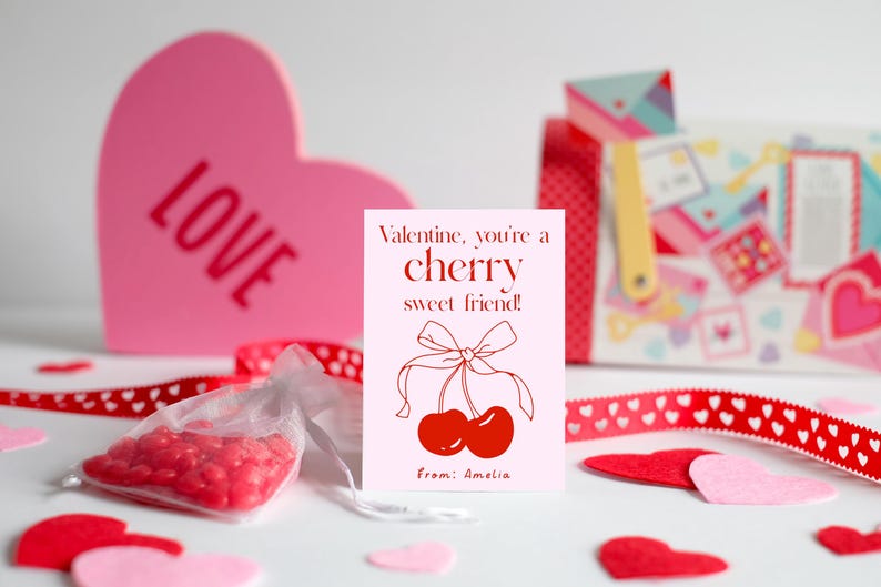 May include: A pink card with red text that reads "Valentine, you're a cherry sweet friend!" with a drawing of two red cherries with a red ribbon. The card is signed "from: Amelia".