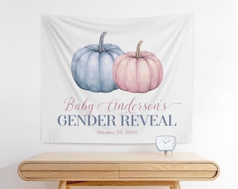 May include: A white fabric banner with watercolor pumpkins in blue and pink. Text reads "Baby Anderson's Gender Reveal" with the date October 29, 2028. A small clock sits on a wooden table.