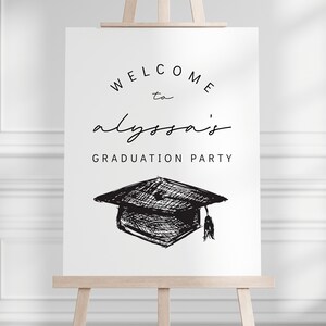 Pu&ograve; includere: Un cartello bianco su un cavalletto di legno con la scritta nera "WELCOME to alyssa's GRADUATION PARTY". Sotto, un disegno in bianco e nero di un cappello di laurea.