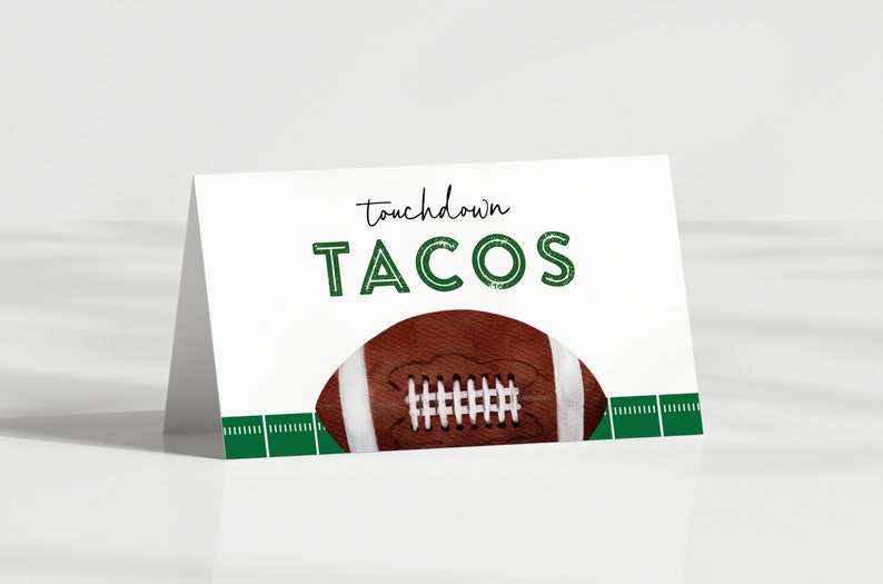 May include: White card with green text that says "touchdown TACOS" with a brown and white football on top of a green and white football field.