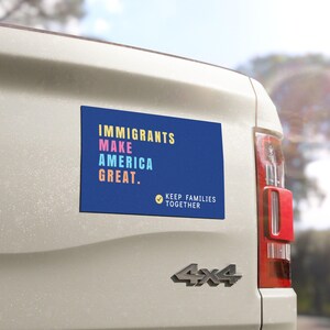 May include: A rectangular blue bumper sticker with the words "IMMIGRANTS MAKE AMERICA GREAT" in yellow, pink, and blue. Below, it reads "KEEP FAMILIES TOGETHER" with a checkmark. The sticker is affixed to a white vehicle.