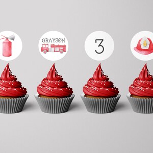 May include: Four cupcakes with red frosting and white sprinkles in grey liners, each topped with a circular paper topper. The toppers feature a red fire extinguisher, a red fire engine with the name GRAYSON, the number 3, and a red fire helmet.