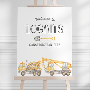 Op de afbeelding: Een welkomstbord voor een bouwthemafeest. Het bord is wit met zwarte tekst die "Welkom op Logans bouwplaats" luidt. Er staat een gele en grijze speelgoedbetonmixer en een gele en grijze speelgoedkraan op het bord. Boven de tekst staat een kleine schop.