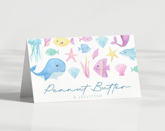 May include: A white card with a watercolor illustration of a whale, jellyfish, fish, seashells, and starfish. The text "Peanut Butter & Jellyfish" is written in blue cursive.