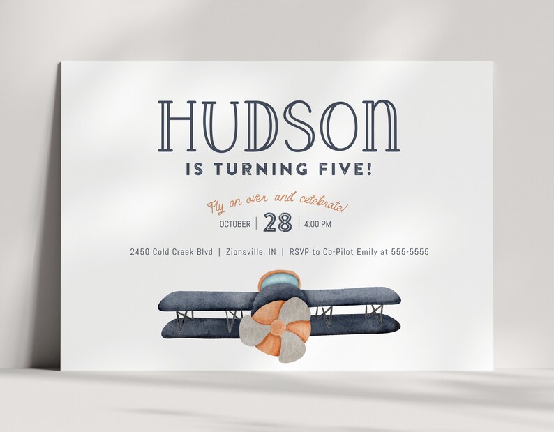 Może przedstawiać: Biała karta zaproszenia z napisem "HUDSON IS TURNING FIVE!" w kolorze granatowym. Karta zawiera tekst "Fly on over and celebrate!" oraz datę 28 października, 16:00. Na dole znajduje się akwarelowa ilustracja dwupłatowca.