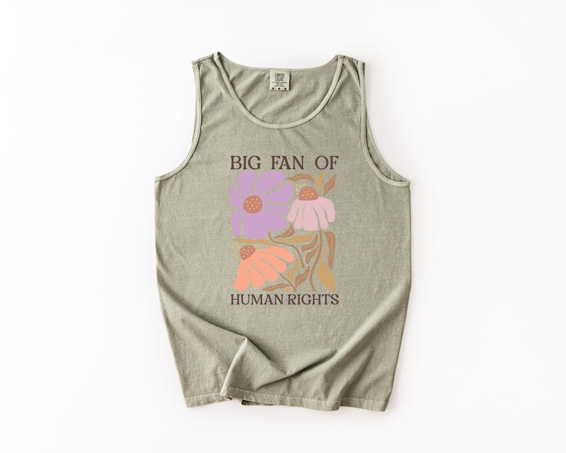 May include: A sage green sleeveless tank top featuring a graphic print of three stylized flowers in shades of purple, pink, and orange. The text "BIG FAN OF HUMAN RIGHTS" is printed in dark brown capital letters above and below the floral design.
