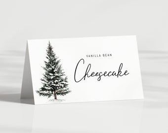 May include: A white card with a snowy evergreen tree illustration and the text "Vanilla Bean Cheesecake" in black script.