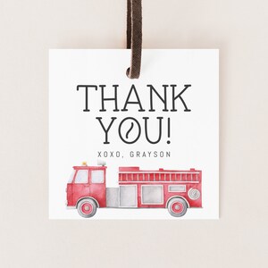 May include: A square white gift tag with a dark brown leather cord at the top. The text THANK YOU! is printed in black, followed by XOXO, GRAYSON. Below the text is a watercolour illustration of a red fire engine with grey accents.