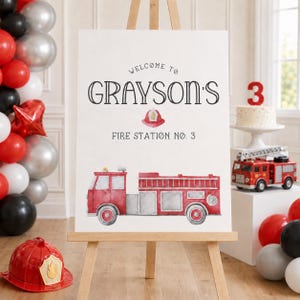 Puede incluir: Un letrero de bienvenida rectangular blanco sobre un caballete de madera con el texto "WELCOME TO GRAYSON'S FIRE STATION NO. 3" en negro, una peque&ntilde;a ilustraci&oacute;n de un casco de bombero rojo y un gr&aacute;fico de acuarela de un cami&oacute;n de bomberos rojo.