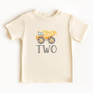 Op de afbeelding: Een cr&egrave;mekleurig T-shirt met een gele kiepwagen en het woord "TWEE" erop gedrukt.