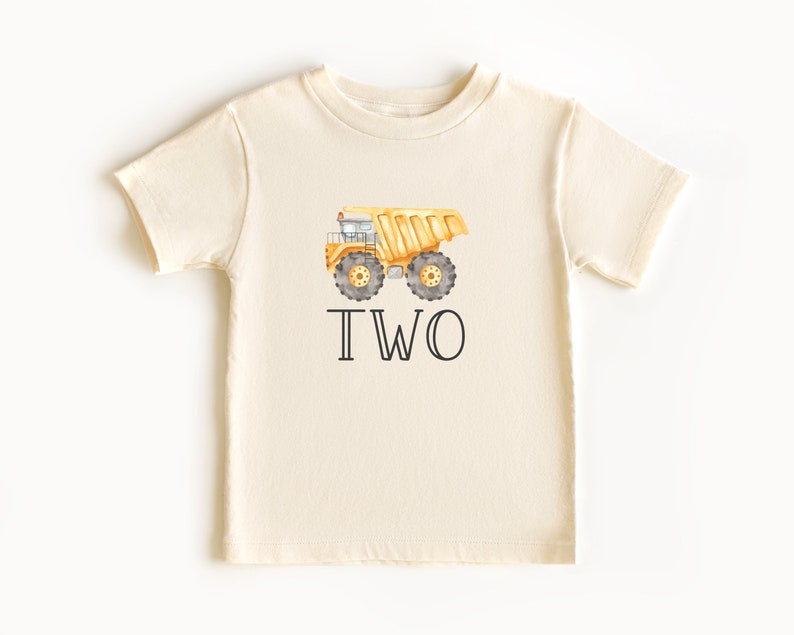May include: A cream colored t-shirt with a yellow dump truck and the word "TWO" printed on it.