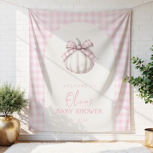 Puede incluir: Un telón de fondo a cuadros rosas y blancos con un diseño de calabaza y lazo en acuarela. El texto "Welcome to Olivia's Baby Shower" se muestra en una elegante escritura. La pancarta cuelga frente a una pared de ladrillos blancos.