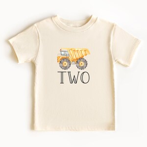 May include: A cream colored t-shirt with a yellow dump truck and the word "TWO" printed on it.