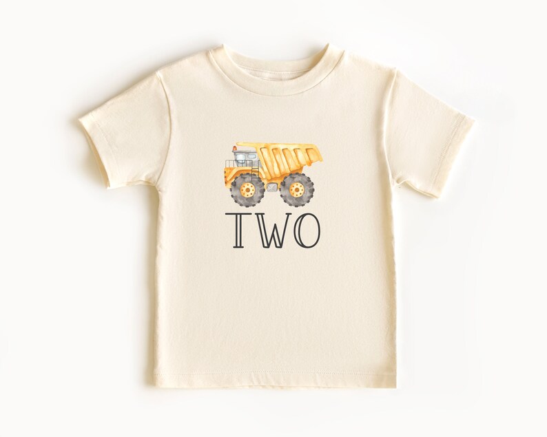 May include: A cream colored t-shirt with a yellow dump truck and the word "TWO" printed on it.