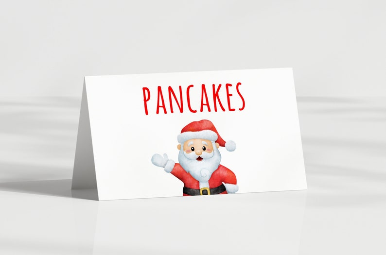May include: A white card with the word "PANCAKES" in red lettering. Below the text is a watercolour illustration of Santa Claus waving. Santa is wearing a red suit, hat, and black belt.