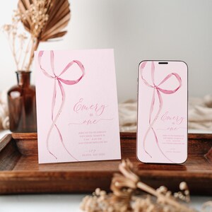 May include: Pink invitation card with a watercolor pink ribbon bow and the text "Emery is one" and details for a first birthday party. A matching invitation is displayed on a smartphone.