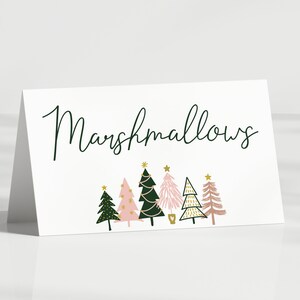 May include: A white card with the word "Marshmallows" written in black cursive script. The card is decorated with six pink and green Christmas trees with gold stars and gold glitter.