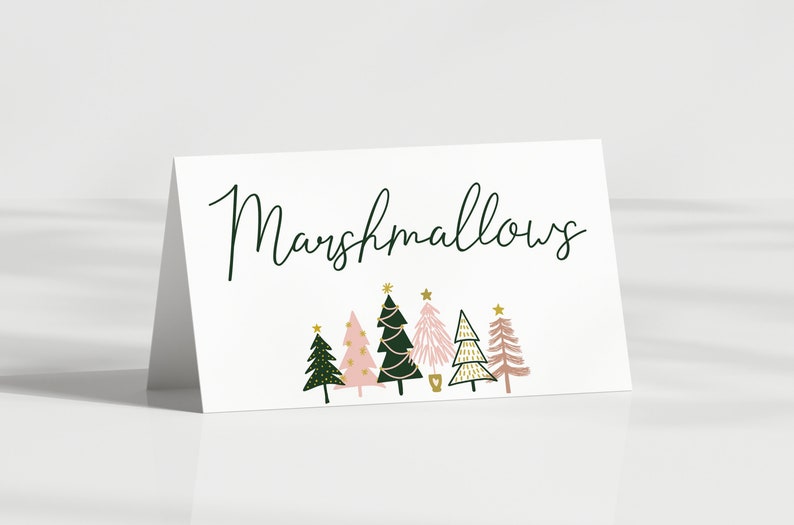 May include: A white card with the word "Marshmallows" written in black cursive script. The card is decorated with six pink and green Christmas trees with gold stars and gold glitter.