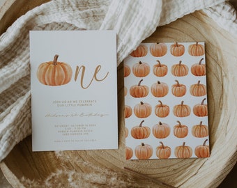 Op de afbeelding: Een witte uitnodigingskaart met een pompoenillustratie en de tekst "one" in gouden letters. De uitnodiging is voor een eerste verjaardag en bevat de tekst "Join us as we celebrate our little pumpkin Hudson's 1st Birthday". De kaart ligt op een houten oppervlak met een witte doek.