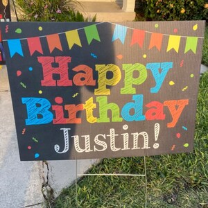 May include: A black chalkboard sign with colorful flags and confetti. The sign says "Happy Birthday Justin!" in colorful chalk-like lettering.