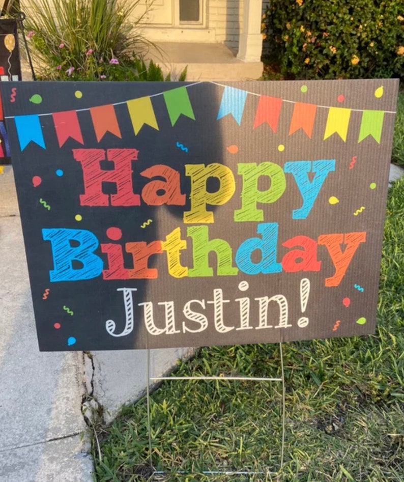 May include: A black chalkboard sign with colorful flags and confetti. The sign says "Happy Birthday Justin!" in colorful chalk-like lettering.