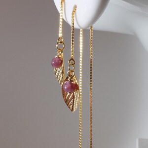 以下が含まれることがあります： 金色のリーフデザインと小さなピンク色のビーズが特徴のぶら下がりピアス。繊細なチェーンからピアスがぶら下がり、優雅な印象を与えます。白いマネキンの頭に表示されています。