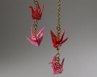 May include: Gold chain earrings featuring origami cranes in red and pink. The cranes are suspended from delicate gold chains, creating a dangling effect. The earrings have a handmade aesthetic, with a focus on Japanese-inspired design.