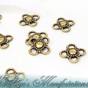 May include: A close-up of a group of gold-toned metal flower-shaped charms with a beaded center. The charms are scattered on a white surface.