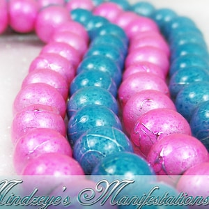 May include: A close-up of a strand of pink and blue beads. The beads are round and have a slightly textured surface. They are arranged in a pattern of alternating colors.