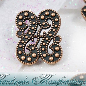 May include: A copper-colored metal charm with a decorative design of two intertwined swirls. The charm is adorned with small, raised dots around the edges and throughout the design.