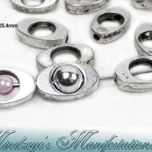 May include: Silver oval-shaped metal beads with different designs. Some beads have a small circle in the center, while others have a small ball or a pearl. 1 inch = 25.4 mm.