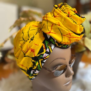 May include: A yellow head wrap with a black and white geometric pattern. The wrap is tied in a knot on top of the head.